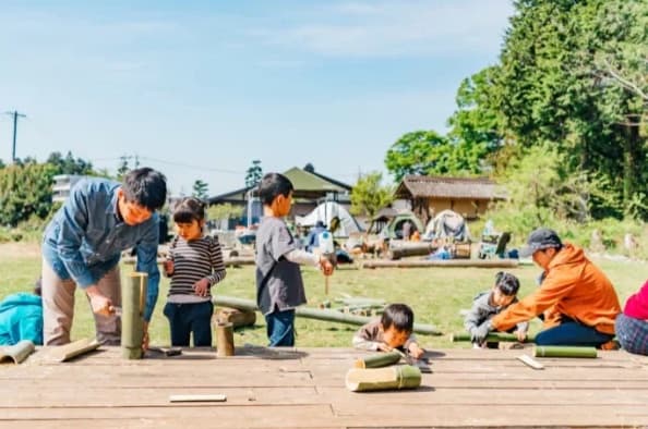 木のデッキの上で、大人と子どもたちが竹を割ったり運んだりしている